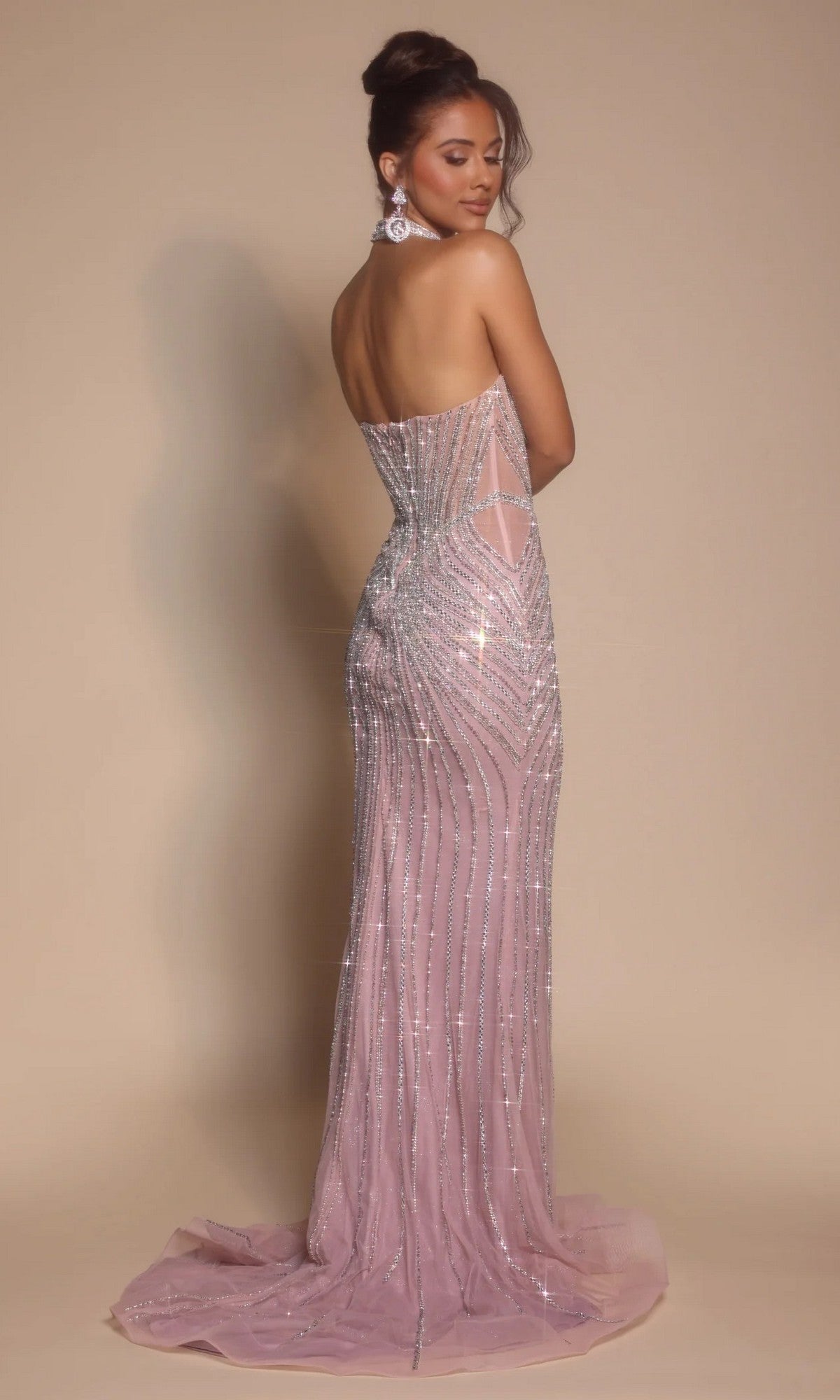 A woman stands slightly turned away against a neutral background, wearing the Portia and Scarlett PS26064 long formal dress—a strapless, floor-length light pink gown with a corset bodice and silver sequin accents.